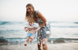 © Halfpoint - Young mother with a toddler boy standing on beach on summer holiday, having fun.