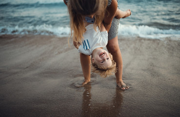 Young mother with a toddler boy standing on beach on summer holiday, having fun.