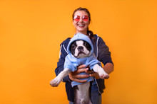 Cute Brunette Woman In White T Shirt And Jeans Holding And Embracing Boston Terrier Dog On Plane Yellow Background. Love To The Animals, Pets Concept.
