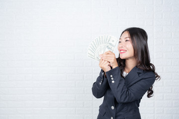 Wall Mural - A young businesswoman holds a dollar note on a white brick wall background.