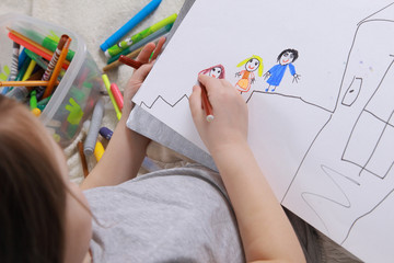 Girl in bright clothing draws a picture of the family. Light room