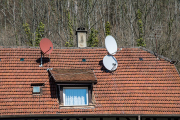 Roof of an old house with many different satellite dishes and a fireplace and a dormer window