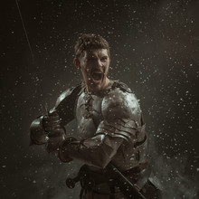 Emotional Portrait Of A Young Man In Knight Armor And A Sword Against A Dark Background.