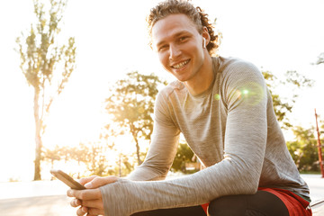 Poster - Confident sportsman wearing earphones sitting outdoors