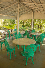 Empty Restaurant Under A White Canopy Among Green Palm Trees With Marble Tables And Green Wrought-iron Chairs