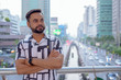 © Ranta Images - Young bearded Indian man thinking on the footbridge against view of the city streets