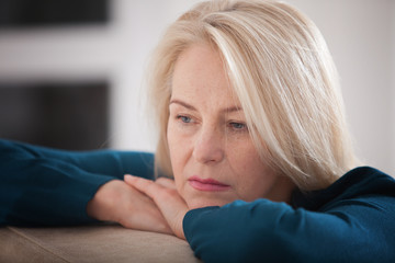 Middle aged woman barefoot sitting on the couch, hugging her head, at home. The concept of sadness and loneliness.