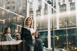 © Maskot - Low angle view of businesswomen using smart phones while standing against modern building in city
