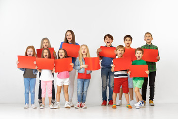 Wall Mural - Group of happy screaming children with a red empty banners isolated in white studio background. Education and advertising concept. Protest and children's rights concepts.