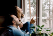 © Maskot - Father and daughter looking through window at home