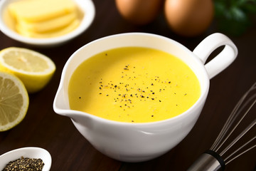 Hollandaise sauce, a basic sauce of the French cuisine, served in a sauce boat with ground black pepper on top, photographed with natural light (Selective Focus, Focus in the middle of the image)