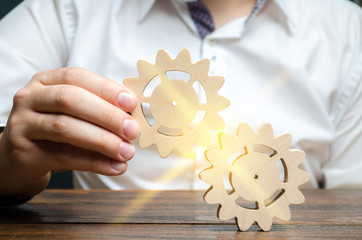 Businessman in white shirt connects two wooden gears. Symbolism of establishing business processes and communication. Increase efficiency and productivity. The best business formula for success.