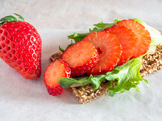 Crisp bread with sesame seeds, lettuce, cheese and strawberry on a white butter paper, close up 