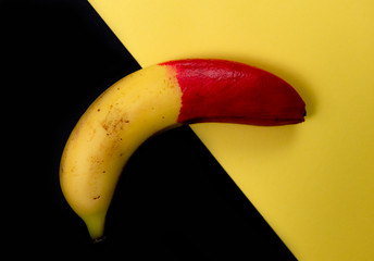 Skin of a fresh banana painted half in red resting on a black and yellow background.