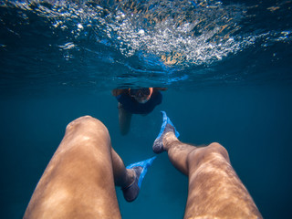 Personal perspective of a male swimming backwards underwater. Young woman following her boyfriend