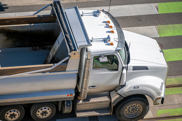 An empty big rig tip truck moves along city street along pedestrian crossing road