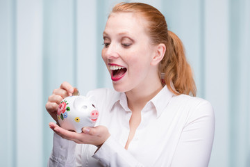 Wall Mural - young red haired woman puts a coin into her piggy bank