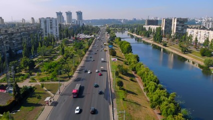 Wall Mural - aerial drone shot town in ukraine road with driving cars along river with blue water beautiful daytime in summer season from left to right