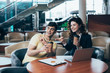 © LIGHTFIELD STUDIOS - smiling customer and car dealer sitting at table in car showroom and holding paper cups