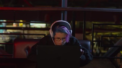 Wall Mural - sequence of videos with young hipster-woman in hoodie and headphones sitting at bar table at laptop,