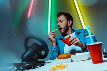 Wall Mural - good-looking and handsome man eating french fries and looking at computer monitor