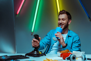 Wall Mural - handsome man holding joystick and drinking soda from paper cup