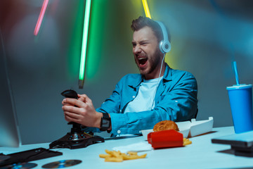 Wall Mural - selective focus of angry cyber sportsman in headphones playing video game with joystick