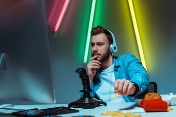 Wall Mural - selective focus of handsome cyber man in headphones looking at computer monitor and eating french fries