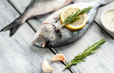 Two fresh raw Dorado fish with spices and olive oil on a wooden table.