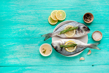 Dorado fish in a plate with spices and olive oil on a wooden table