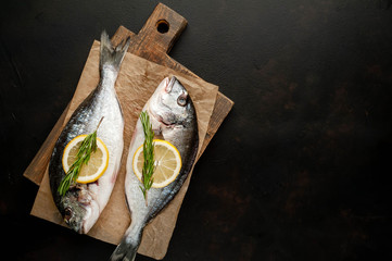 two fresh raw Dorado fish on a cutting board with spices and olive oil on a stone background. Space for text