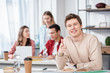 © LIGHTFIELD STUDIOS - Smiling student with book sitting at table and pointing with finger at camera