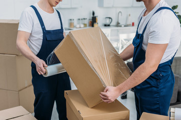 Wall Mural - partial view of movers wrapping cardboard box with stretch film in apartment