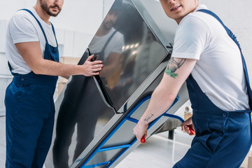 cropped view of two movers using hand truck while transporting refrigerator in apartment