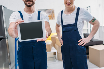 cropped view of two movers presenting digital tablet with blank screen in apartment