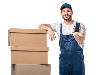 Sticker - handsome smiling mover with cardboard boxes presenting smartphone with blank screen isolated on white