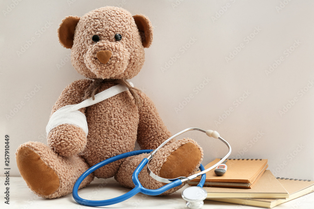 Toy bear with bandage, stethoscope and stationery on table