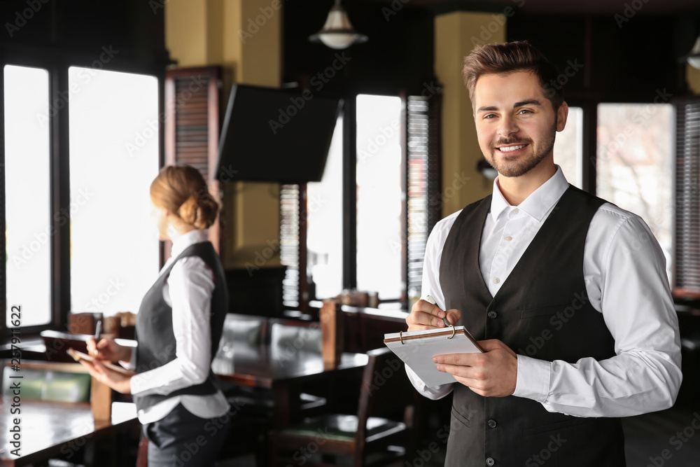 Young male waiter with notebook in restaurant