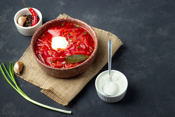 Wall Mural - Vegetarian beet red soup - borscht with sour cream on black stone background. Top view.