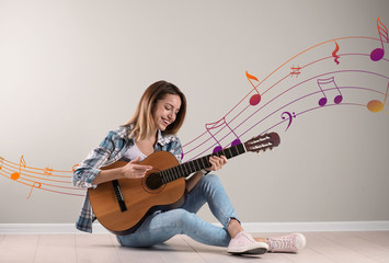 Wall Mural - Young woman playing acoustic guitar near grey wall