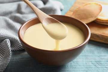 spoon of pouring condensed milk over bowl on table, closeup. dairy products