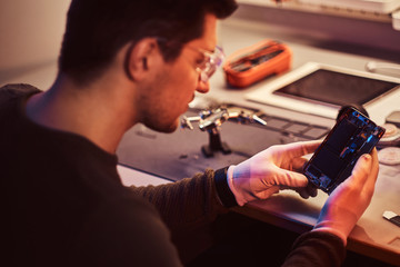 Wall Mural - The technician carefully examines the integrity of the internal elements of the smartphone in a modern repair shop