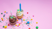 Two Birthday Cupcakes With Candles On Pink Pastel Background, Copy Space.