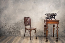 Vintage Loft Room With Old Typewriter On Wooden Table And Antique Chair Front Concrete Wall Background With Shadows. Retro Style Filtered Photo
