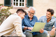 © Westend61 - Three happy men of different age using laptop in garden