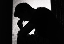 Silhouette Of Young Man Feeling Sad, Tired Sitting In A Dark Room