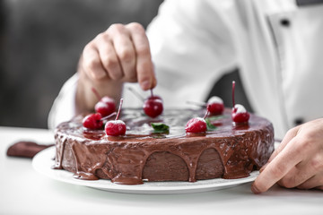 Male confectioner decorating tasty chocolate cake in kitchen, closeup