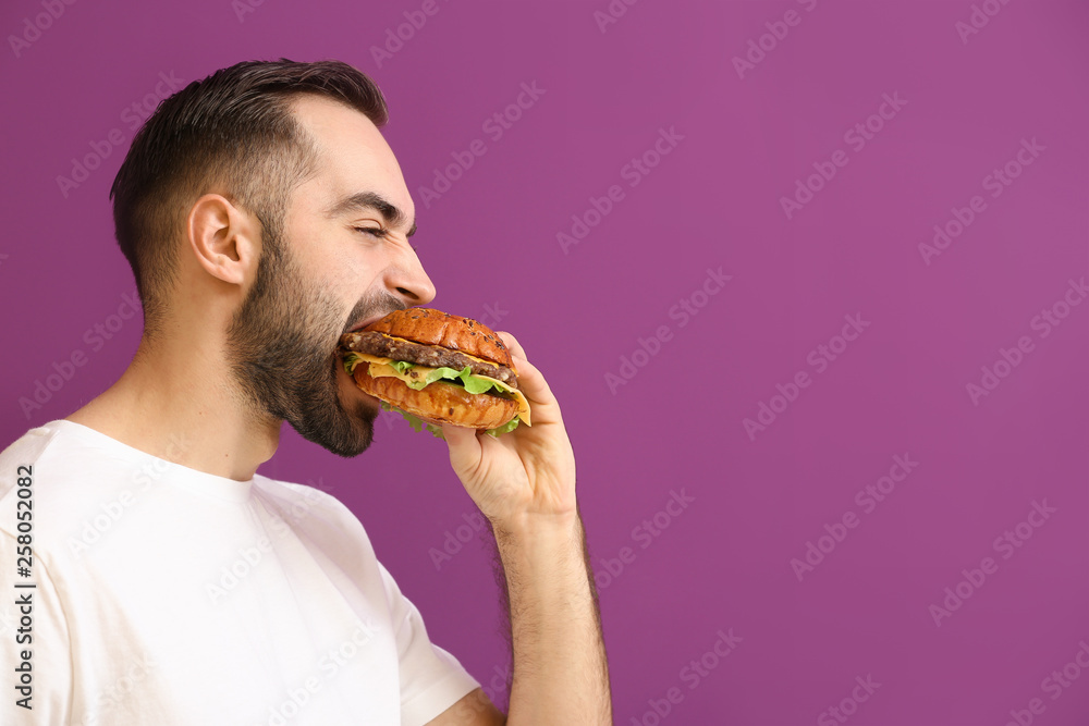 Man eating tasty burger on color background