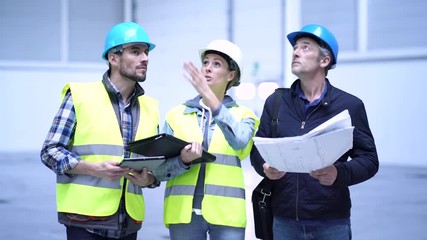 Wall Mural - Mixed team of construction workers talking over plan in warehouse 