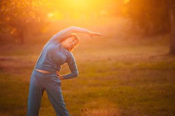 An elderly woman goes in for sports at sunset.